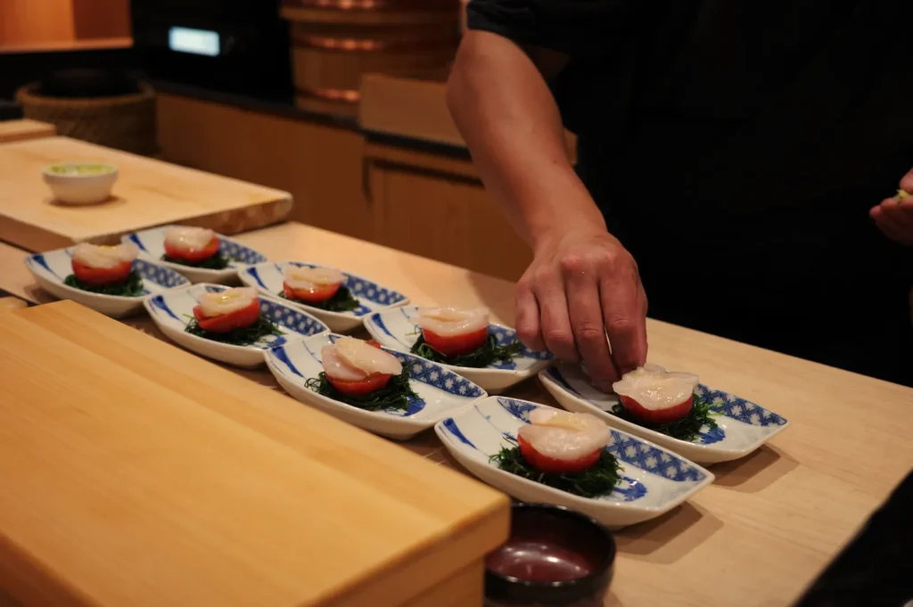 A chef plating sushi on small blue and white plates arranged on a wooden counter.