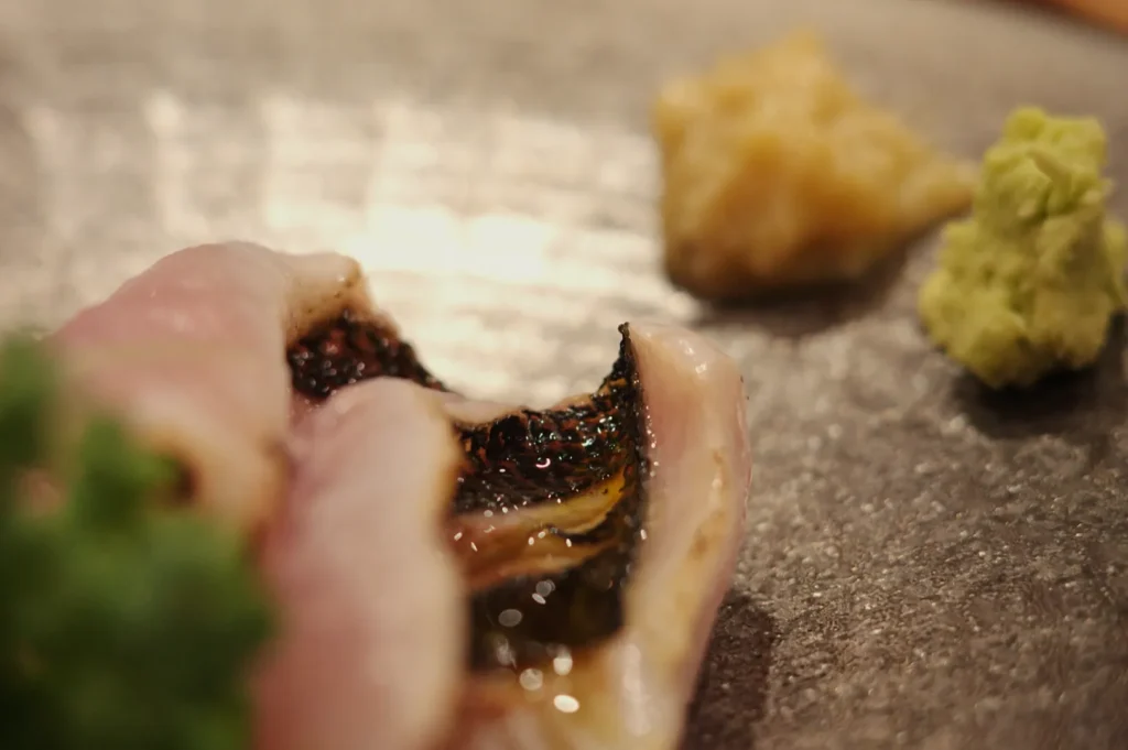 A close-up of sushi with sliced fish, accompanied by wasabi and ginger on a dark plate.