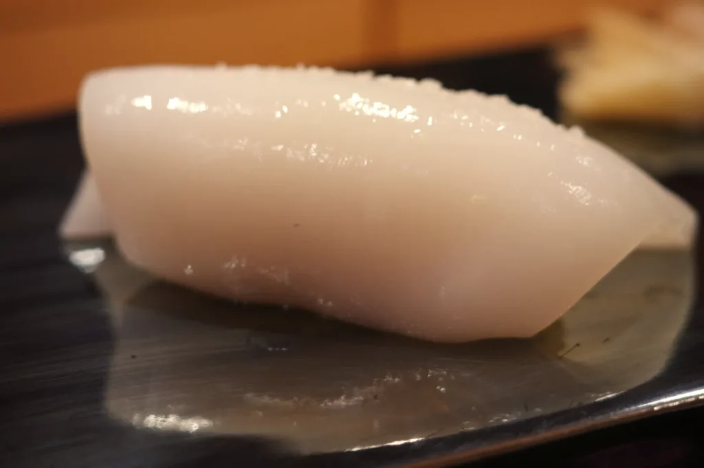 A piece of sushi featuring a translucent, white slice of seafood on a metal platter.