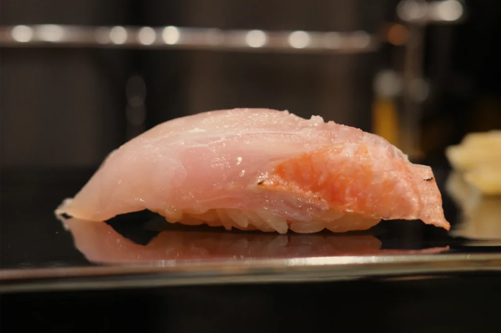 Close-up of pink salmon nigiri sushi on a glossy black plate, its delicate fish topping glistening under warm restaurant lighting.
