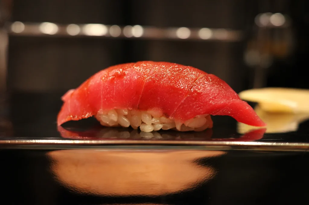 A piece of sushi with a red slice of tuna on top of a small mound of rice.