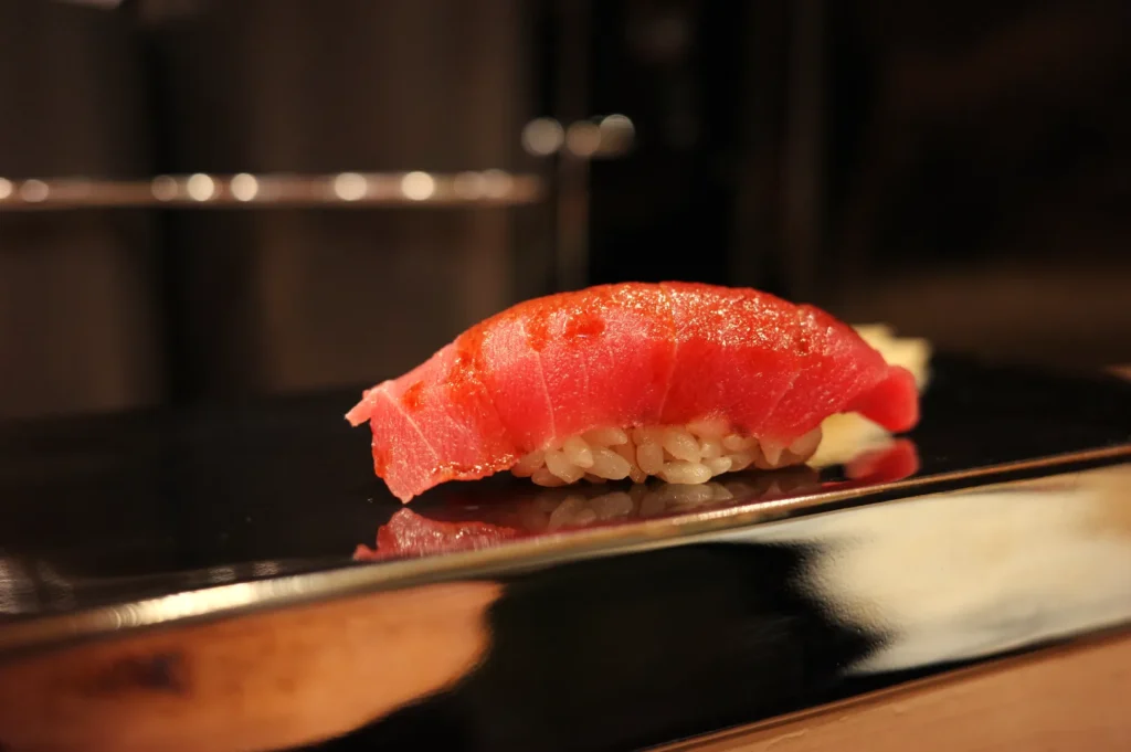 A piece of sushi featuring a slice of raw fish on top of rice, sitting on a polished surface.
