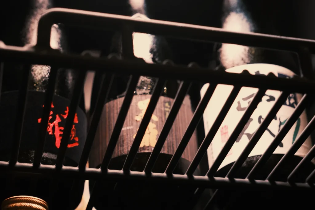 Close-up of black metal shopping cart bars against warm sunlight, with blurred graffiti and urban textures creating a moody, gritty atmosphere.