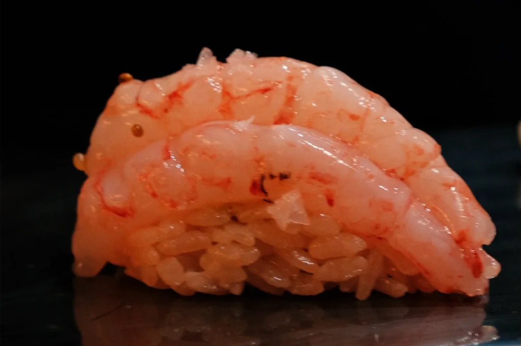 A piece of sushi topped with pink shrimp over a mound of vinegared rice.