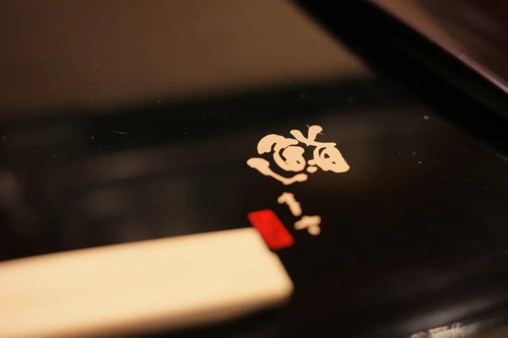 A close-up of a decorative design on a black surface, featuring a stylized character and a piece of a chopstick.