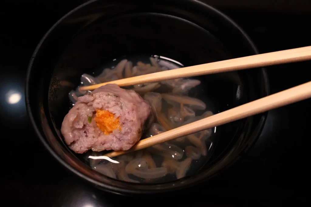 A bowl of clear broth with a piece of dumpling held by chopsticks.