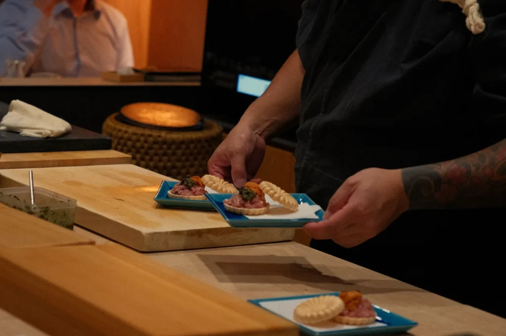 A chef holding two plates of food, each with small appetizers, in a kitchen setting.