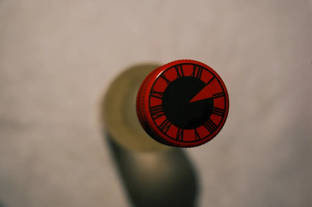 A top view of a bottle with a circular red and black cap featuring clock-like markings.