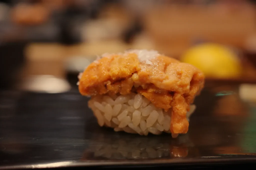 A piece of sushi topped with orange sea urchin (uni) sitting on a small mound of rice.