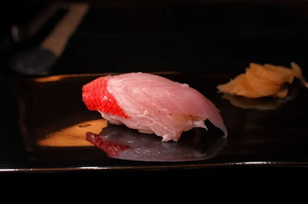 A piece of sushi on a black plate, featuring a slice of fish on top of rice, accompanied by a small amount of pickled ginger.