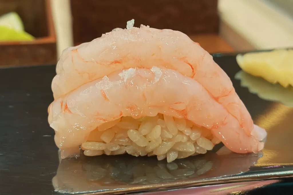 A piece of sushi with two layers of translucent pink shrimp on top of a mound of rice.