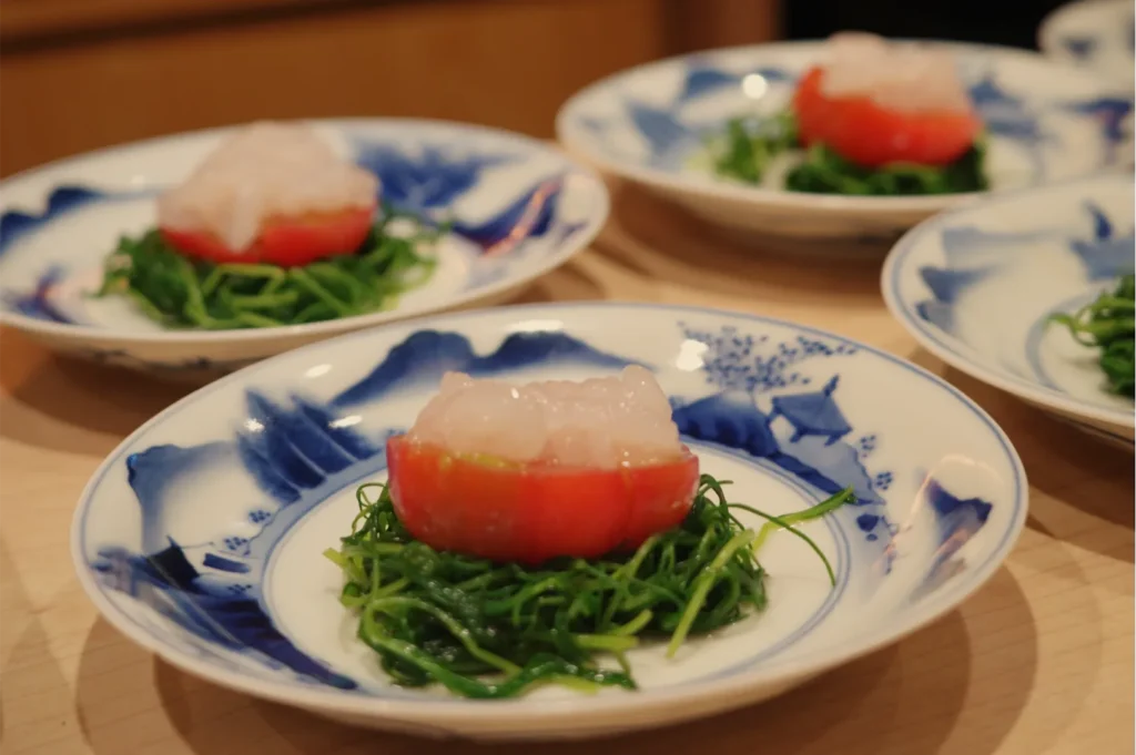 Blue-and-white dishes hold red-and-white seafood atop shredded green seaweed, arranged on a wooden table, creating an elegant Japanese meal.