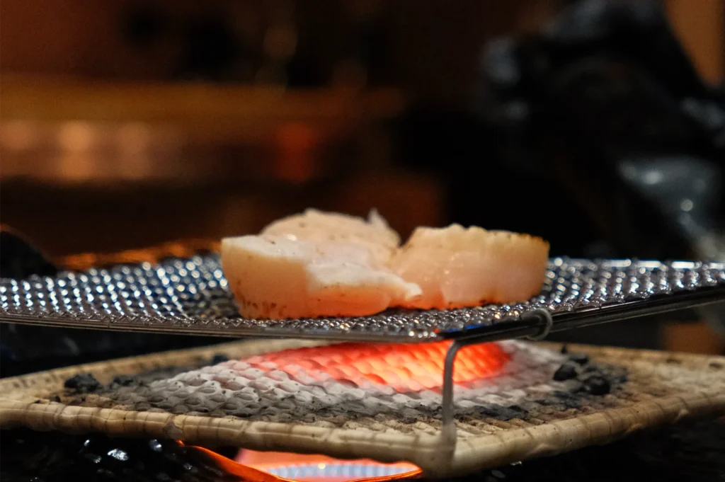 Sliced fish fillets grilling on a metal rack over glowing charcoal.