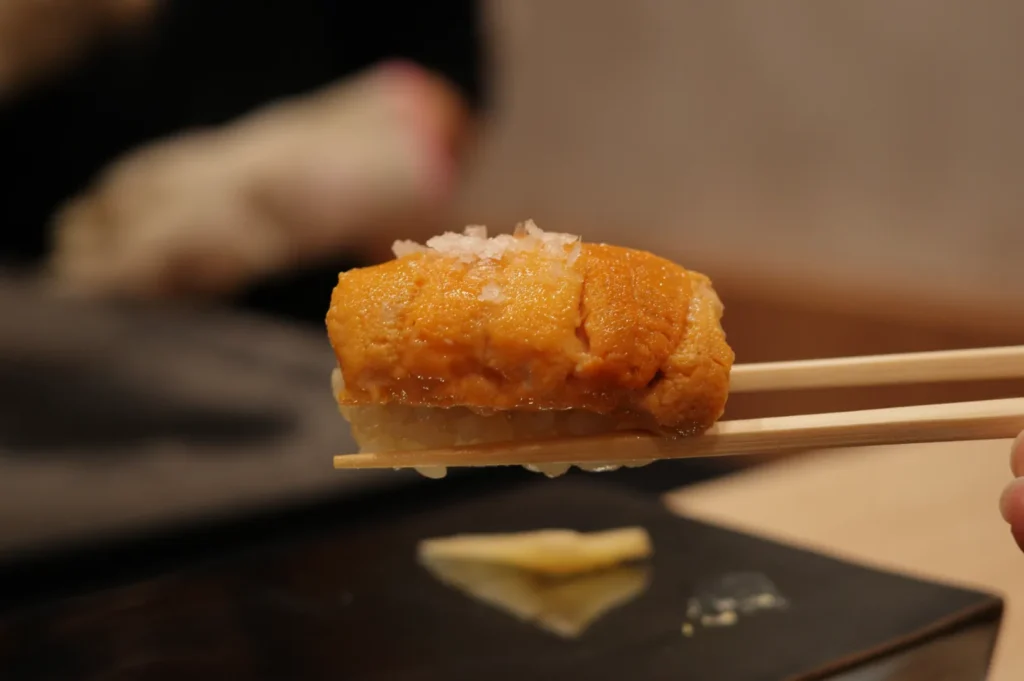A piece of sushi held with chopsticks, featuring a mound of uni (sea urchin) on top of a rice ball.
