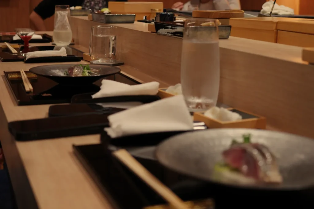 A dining table set with utensils, black plates, and a glass of water, featuring sushi or sashimi, in a restaurant setting.