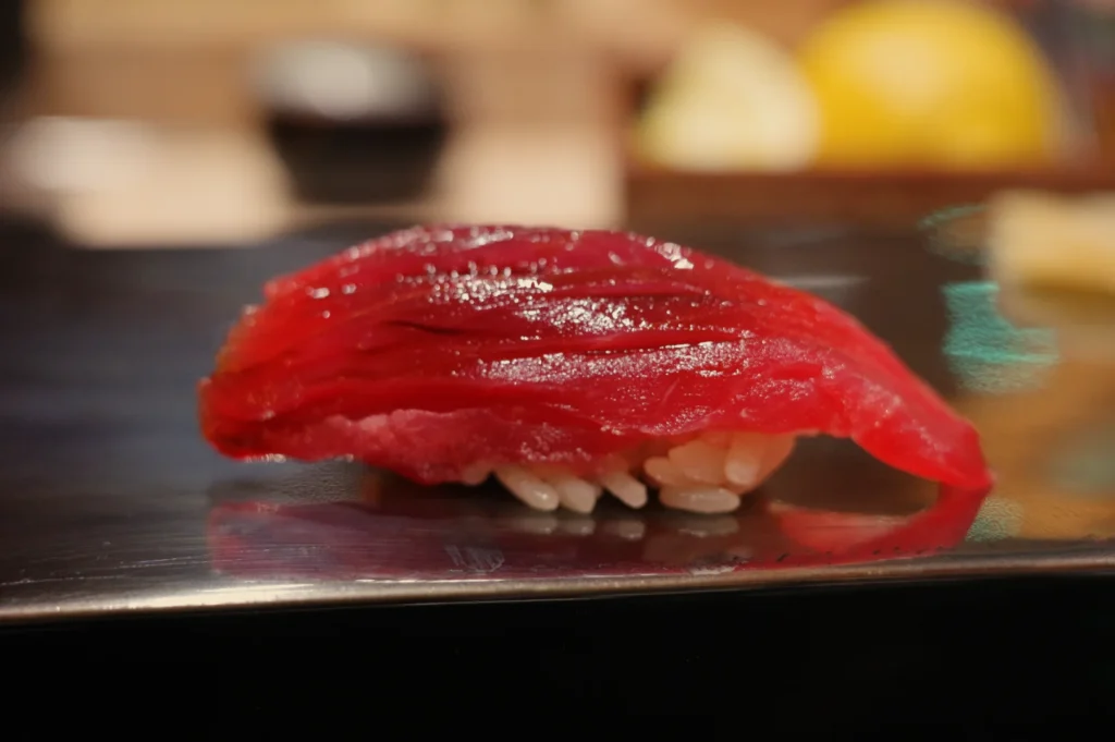 Close-up of glossy red tuna nigiri sushi on a dark plate, with rice peeking beneath the fish; warm, softly blurred restaurant lighting creates an inviting mood.