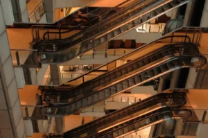 A maze of parallel escalators crisscrosses a multi-level indoor atrium, glowing with warm amber light and creating a dramatic, industrial atmosphere.