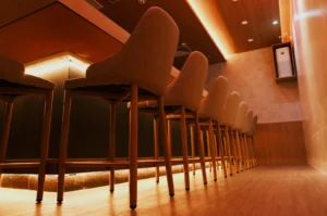 Low-angle view of cushioned bar stools lined along a polished wooden counter in a warmly lit, elegant lounge, creating an intimate, inviting mood.