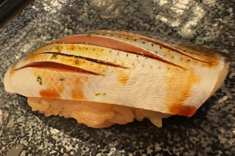 Close-up of seared salmon nigiri on a dark speckled plate, with browned scoring, orange edges, and rice beneath; warm and appetizing.