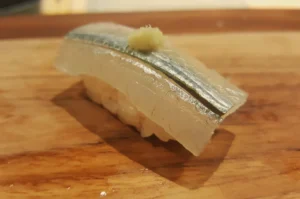 Close-up of silver-skinned fish nigiri sushi with a small dab of garnish on a wooden board; warm lighting gives the scene an inviting feel.