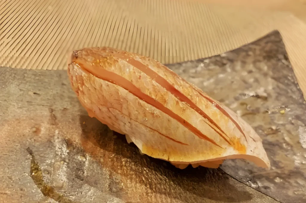 A golden-brown loaf of crusty bread rests on a stone baking surface, its long split top revealing a warm, rustic crumb in soft light.
