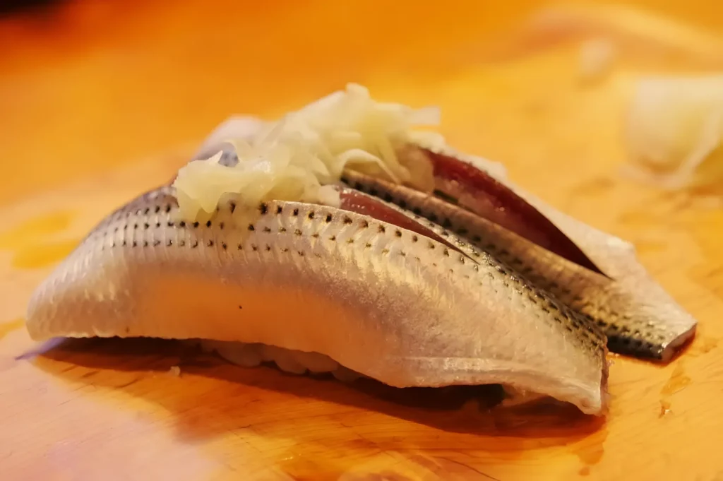 Close-up of grilled fish fillets topped with chopped onions on a wooden board, their golden-brown skin creating a warm, appetizing food scene.