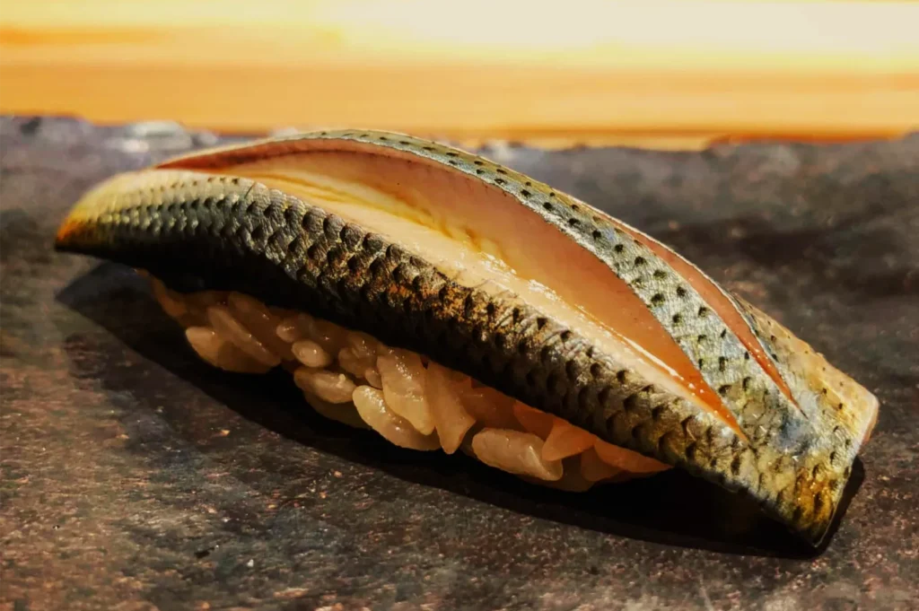 A close-up of a sliced sea cucumber showing its orange interior and rows of pale tube feet, resting on dark rock beneath a warm, hazy sky.
