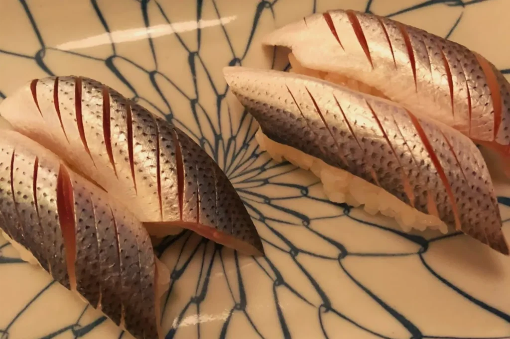Two browned, scored pieces of fish lie on a cream plate with a dark blue branching pattern, creating a warm, appetizing food presentation.